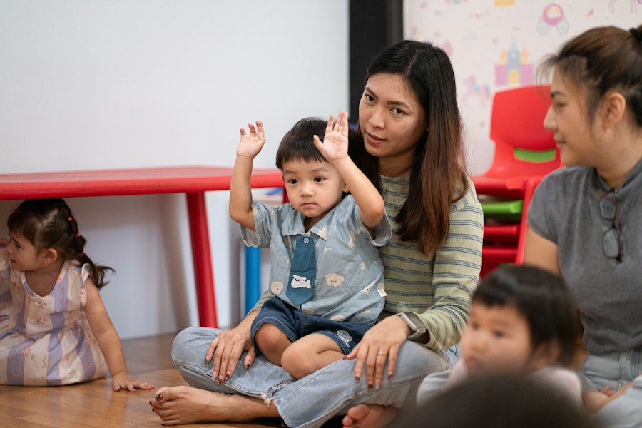 An educator sitting on the floor with a toddler who raises his hands